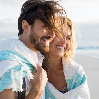 Happy couple wrapped up in blanket on the beach
