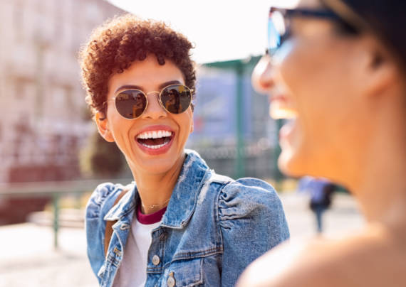 Young brazilian woman wearing sunglasses smiling at friend on the street.