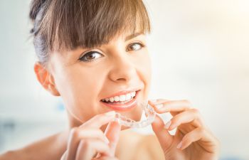 A woman with perfect smile holding an Invisalign aligner